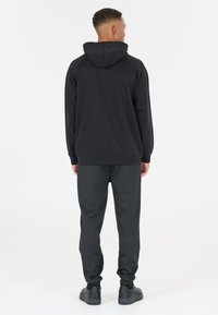 Svart hoodie med huva, raglanärmar och ribbade ärmslut, tillsammans med mörkgrå sweatpants och svarta sneakers. Enkel design, mjuk textur.