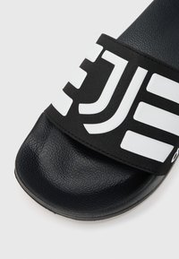 Sort sandle med glidende sål, der har et tekstureret bånd med fed, hvid skrift, og en glat, sort fodseng for komfort.