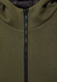Olivgrüne Reißverschlussjacke aus strukturiertem Strickstoff mit schwarzem Reißverschluss. Verfügt über eine Kapuze und ein glattes Innenfutter.