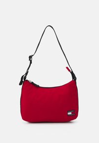 Bolso de hombro de nailon rojo con una correa negra, forma redondeada, cierre de cremallera y un parche con el logotipo "TOMMY JEANS" en la parte frontal.