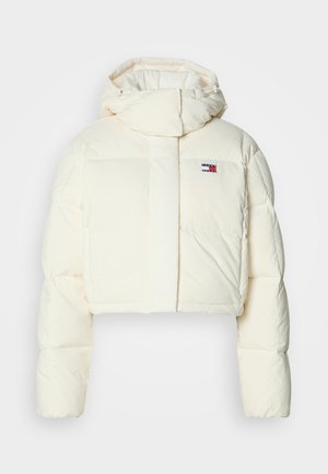 Cropped, cream puffer jacket with a high collar and zipper hood. Features a rectangular patch logo on the chest and quilted sections.