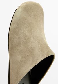 Mule en daim beige avec bout arrondi et dos ouvert, vue de dessus sur fond blanc.