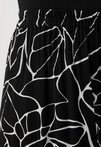 Black pleated skirt featuring a white abstract pattern, with an elastic waistband for comfort and textured fabric.