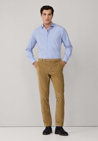 Lichtblauw gestreept overhemd met lange mouwen, gecombineerd met tan corduroy broeken. Donkerblauwe schoenen maken de outfit compleet.