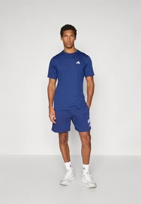 Marineblåt atletisk t-skjorte og shorts laget av lett stoff, med en liten hvit logo på brystet og shorts med sidelommer.