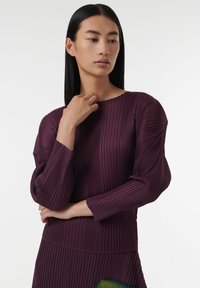 Top largo de manga larga en color ciruela, con tejido texturizado, escote redondo y detalles fruncidos en los hombros. Acabado suave y diseño en capas.