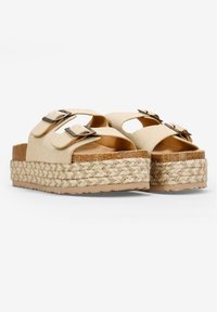 Sandalias de plataforma beige con doble hebilla, parte superior de tela suave, entresuela de cuerda de yute y suela de goma texturizada. Forma redondeada con la parte delantera abierta.