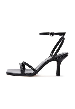 Sandalia negra de tacón alto con tiras finas, punta cuadrada y correa en el tobillo con hebilla plateada sobre fondo blanco.