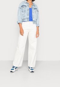 Světle modrá džínová bunda, zkrácený střih, se dvěma předními kapsami; spárována s modrým tílkem a bílými širokými džíny. Bílé a modré tenisky.