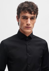 Black dress shirt made of smooth fabric, featuring a structured collar, front button closure, and fitted design.