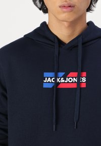 Navy blue hoodie made of soft fabric, featuring a logo with blue, red, and white elements. Includes drawstrings and a front pocket.
