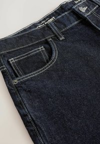 Tumed sinised denim püksid keskmise kõrguse vöökohaga, kontrastsete valgete õmblustega, viie tasku disainiga ning metallist nupuga kinnitamine.