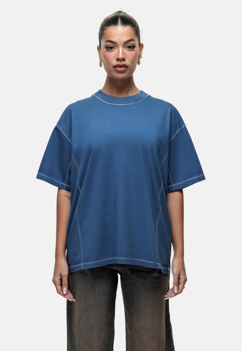 Overmaat blauwe katoenen t-shirt met korte mouwen, ronde hals en contrasterende stikdetails. G gedragen met donkere, losse broek.