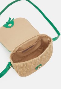Tkaný slámový crossbody batoh, béžový exteriér s texturovaným povrchem, zelené kožené detaily, zlatý tón zapínání na špendlíky a béžová textilní podšívka.