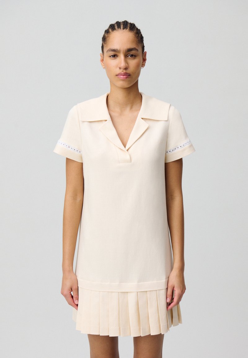 Vestido de color crema de manga corta con cuello, que presenta una falda con pliegues y acentos de encaje en las mangas. Textura suave, ajuste relajado.