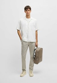 Witte T-shirt met korte mouwen, lichtgrijze broek, beige rugzak met een gladde textuur en verstelbare banden, gecombineerd met beige sneakers.