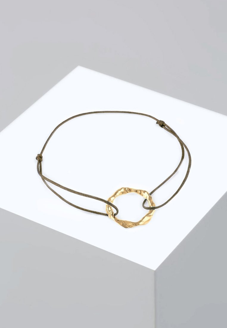 Goldfarbener Metallarmreif mit einem strukturierten, runden Anhänger an einem verstellbaren braunen Band, das ein minimalistisches Design zeigt.