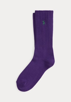Une seule chaussette crew violette avec une partie supérieure côtelée et un petit logo vert brodé près du haut.