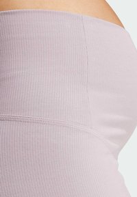 Närbild av ett ljuslila ribbat tygmammaband som är sträckt över en gravid mage, vilket visar sömnadsdetaljer och textur.