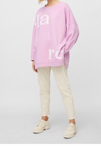 Sudadera rosa de gran tamaño con texto gráfico blanco, que presenta un cuello redondo y hombros caídos, combinada con pantalones beiges claros y zapatillas color crema.