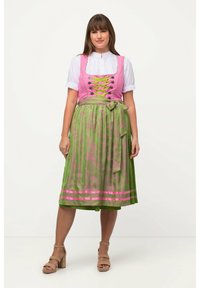 Abito tradizionale dirndl con un corpetto rosa, blusa bianca e gonna verde con motivi floreali e strisce rosa. Sandali chunky con tacco marrone.