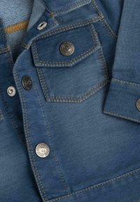 Chemise en denim de couleur bleu foncé, dotée d'une poche poitrine, de boutons en argent, de coutures jaunes contrastantes et d'une texture douce.