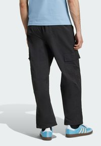 Czarne spodnie cargo o luźnym kroju, z bocznymi kieszeniami i teksturowanym materiałem. W zestawie z niebiesko-białymi trampkami.