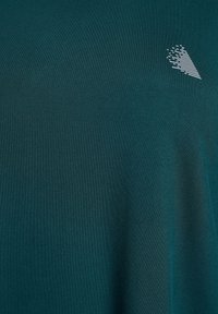 Tmavomodrozelená látka s malým bielym šikmým prúžkovým logom blízko pravého horného rohu, pripomínajúcim štýlovú šípku alebo trojuholník.