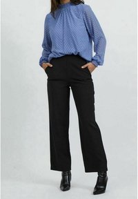 Blusa azzurro chiaro con un motivo a zigzag, colletto arricciato e maniche a sbuffo, abbinata a pantaloni neri a vita alta e stivaletti neri.