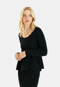 Blusa negra de manga larga con cuello redondo, que presenta adornos plateados dispersos. El detalle de peplum añade una forma acampanada.