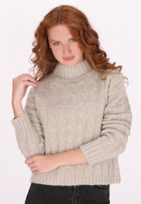 Jasno beżowy sweter w sploty z wysokim ribbowanym kołnierzem i długimi rękawami, z teksturowanym wzorem. Miękki, przytulny materiał.