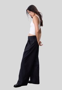 Pantalons à pinces larges en tissu bleu marine foncé. Texture lisse, taille haute avec plis, associés à un débardeur blanc ajusté.