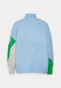 Pull à col roulé bleu clair avec des blocs de couleurs géométriques gris et verts sur les manches, vu de dos.