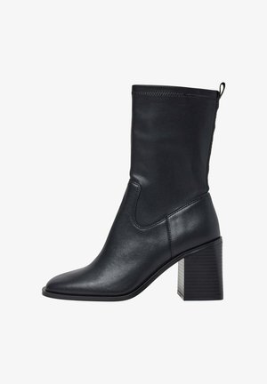 Črne usnjene gležnjarje z kvadratnim nosom in blokastim peto. Gladka tekstura, raztegljiv zgornji del in zanka na zadnji strani za enostavno obuvanje.