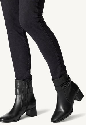 Bottines en cuir noir à talon carré, avec une fermeture éclaire sur le devant, des accents de larges bandes et un détail texturé en haut.
