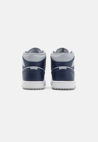 Středně vysoké tenisky s tmavě modrým koženým svrškem, šedými akcenty a bílou gumovou podrážkou. Obsahují vyšitý detail loga na patě.