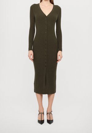 Femme portant une robe en maille côtelée olive, ajustée, à manches longues, avec des boutons sur le devant et des talons noirs à bout pointu.