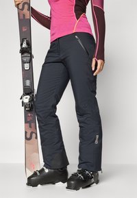 Pantaloni da sci neri, realizzati in materiale impermeabile, con tasche con zip, polsini rinforzati e logo Colmar sul lato.