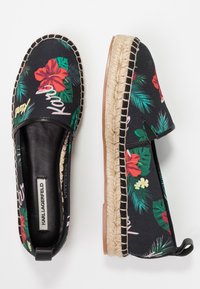 Espadrilles negras con un estampado floral tropical, con una suela de cuerda texturizada, lados elasticados y detalles en cuero. Marca visible en el interior.