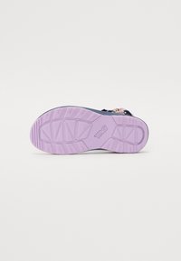 Lilla gummi yttersåle med teksturert såle, merket med "Teva." svarte stropper med blomstermønster på oversiden.