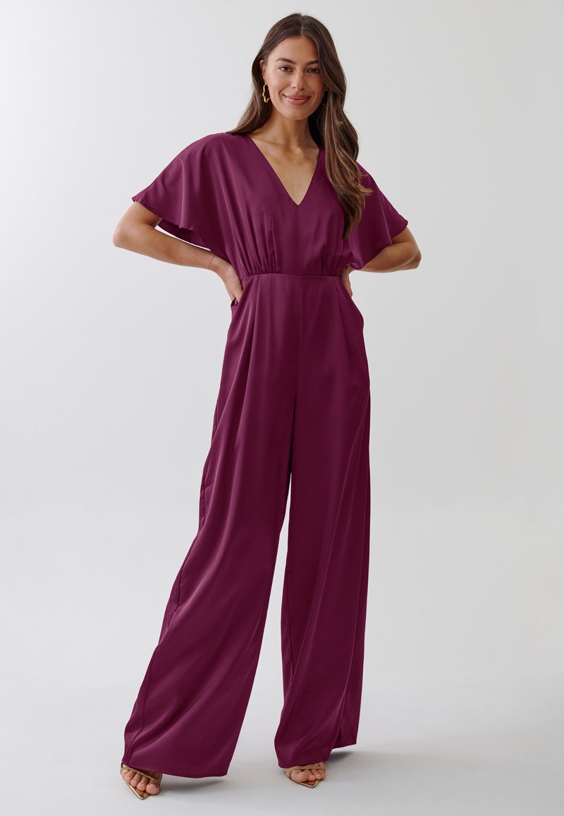 Jumpsuit v slivkovej farbe s výstrihom do V, krátkymi volánovými rukávmi, priliehavým pásom a širokými nohavicami, vyrobený z hladkej, ľahkej tkaniny.