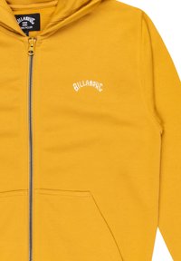 Felpa gialla con zip realizzata in tessuto morbido, dotata di tasca frontale e logo ricamato sul petto a sinistra. Texture liscia, design casual.
