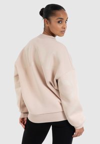 Sweatshirt oversize rose clair avec de grandes lettres discrètes dans le dos, des poignets côtelés et un col rond. Tissu doux et texturé.