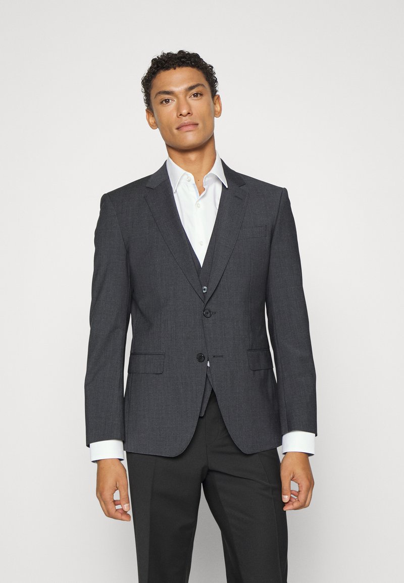 Mörkgrå blazer med två framfickor, enkel knappstängning, slagkrage och vit skjorta synlig under. Skräddarsydd passform.