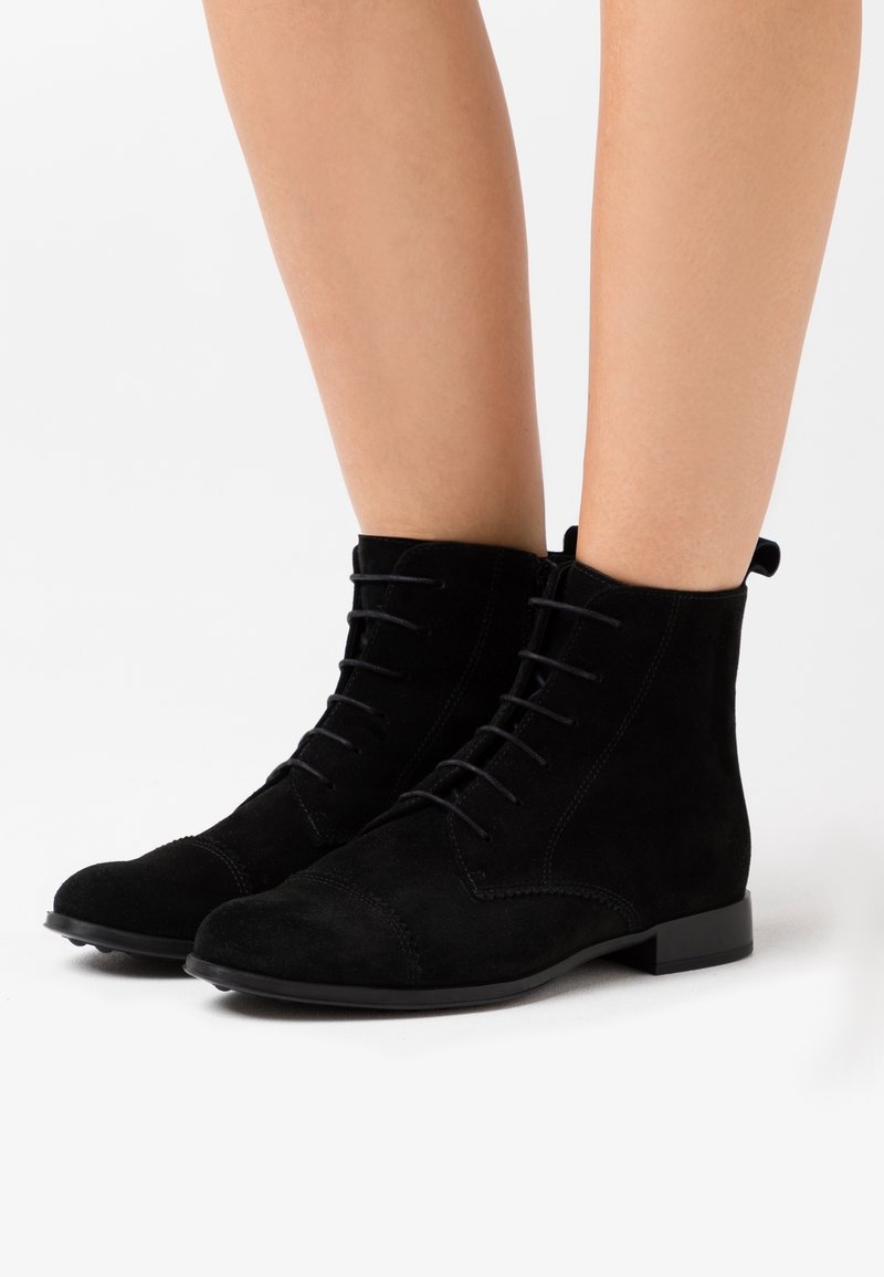 Bottines en daim noir à texture lisse, bout rond, design à lacets, et talon plat bas. Les bottines présentent des accents de surpiqûres et une languette à l'arrière.