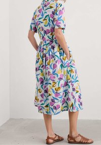 Bloemrijke jurk met korte mouwen en een kraag, met een lavendel-, gele en groene print op een lichtblauwe achtergrond. Inclusief zakken.