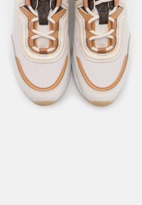 Baskets avec une tige en mesh blanc, des accents en cuir beige, une languette marron texturée, des lacets beige et une semelle en caoutchouc.