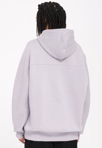 Sweat à capuche violet clair en tissu doux, avec des épaules tombantes et une coupe décontractée. Design minimaliste avec des poignets et un ourlet côtelés.