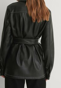 Chaqueta de cuero negra con cintura ceñida y un acabado suave, costuras en contraste y un corte relajado. Detalles de botones en las mangas.