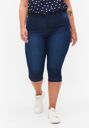 Dark blue denim capri jeans with a fitted design, mid-rise waist, and minimal stitching details, paired with white sneakers.